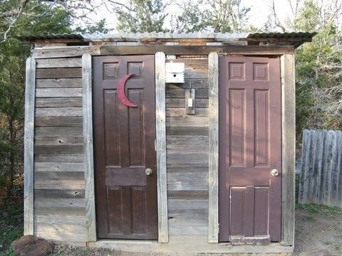 Two outdoor wooden outhouse doors, one with a crescent moon cutout, against a weathered shed wall.
