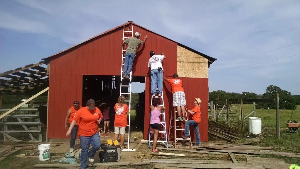 Workers painting a red barn, using ladders outside on a farm.