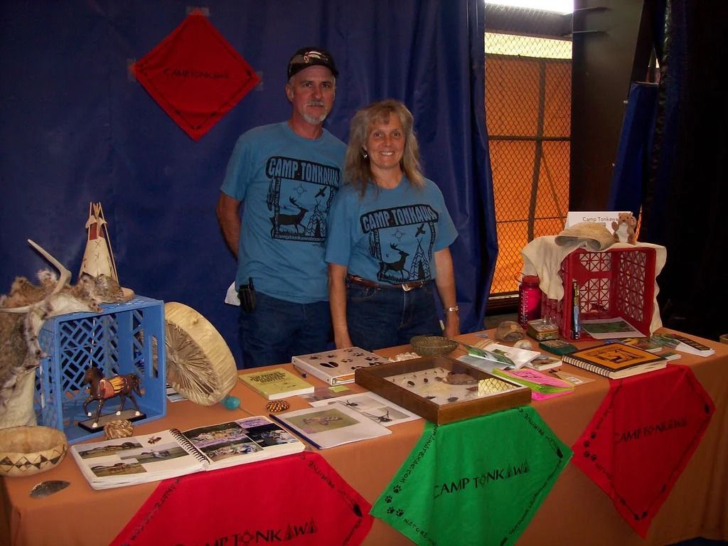 Two people behind a display table with craft items, decorated with red and green cloths and ornaments.