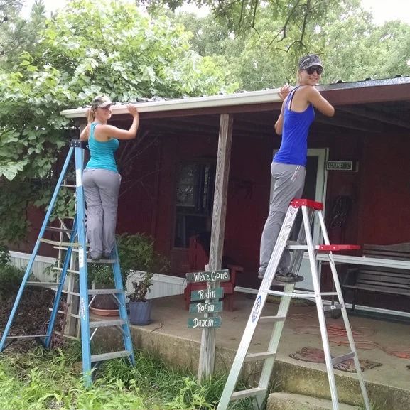 Two people on ladders painting the trim of a house porch outdoors