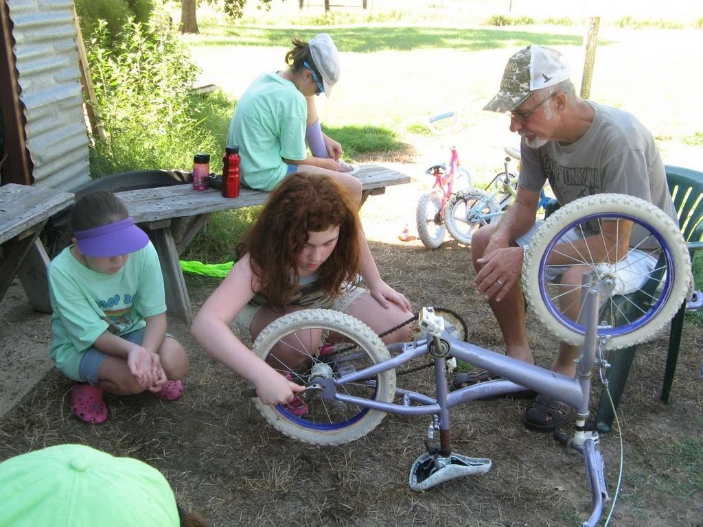 People repairing a bicycle outdoors, with tools and parts spread around them.