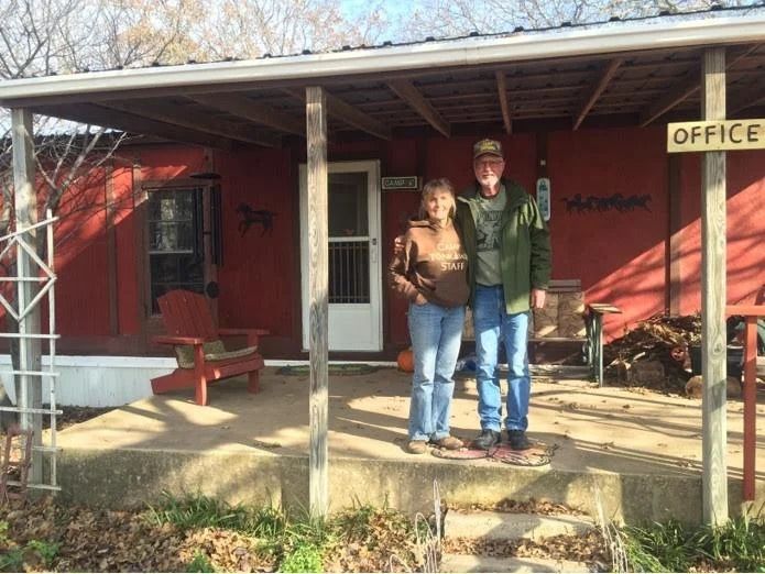 Two people standing on a porch outside a red building labeled “Office”