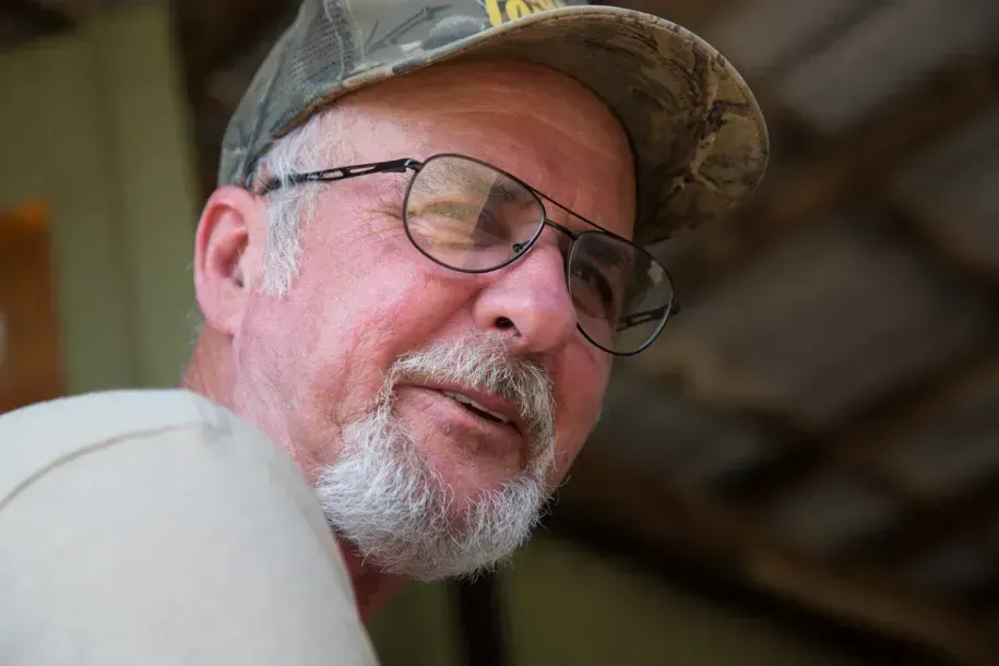 Close-up of a smiling man in glasses and a camouflage cap indoors