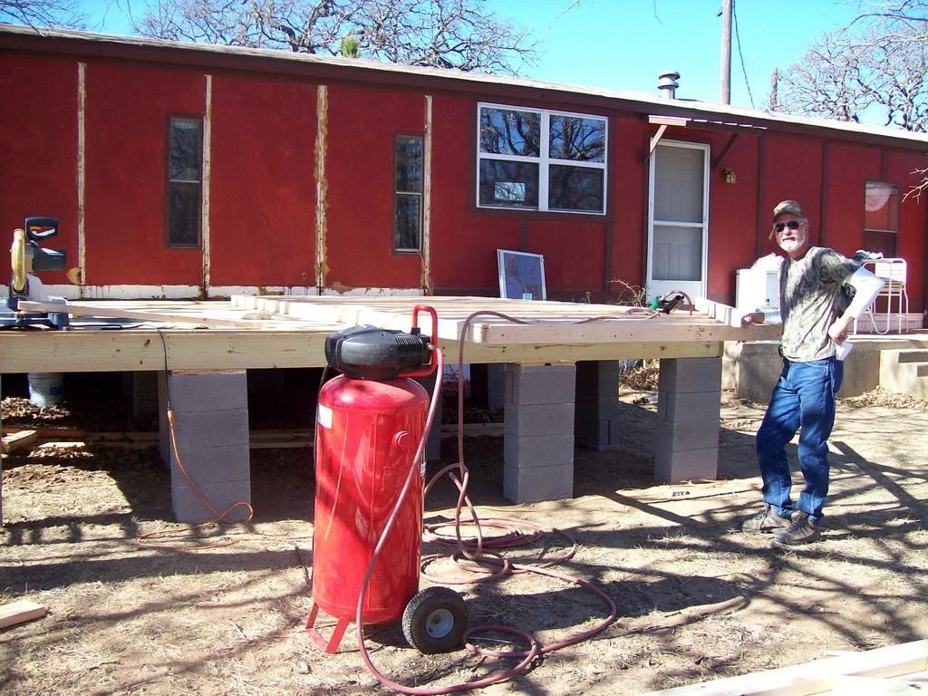Red building with a raised wooden platform, a red tank in front, and a person standing on the right side.