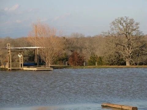 Calm lake with rippling water, a small dock, and bare trees along the shoreline under a clear sky.
