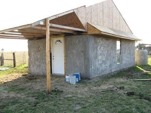 Small unfinished gray house with a wood porch and white door in a rural field.