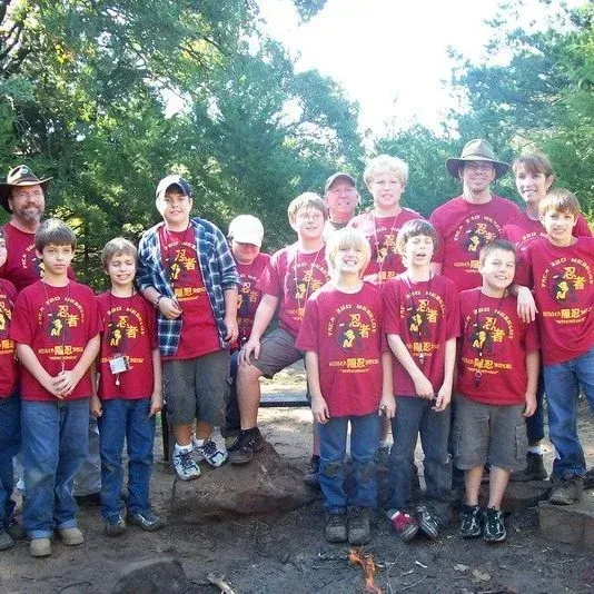 Group of campers in matching red shirts posing outdoors on rocks in a wooded area
