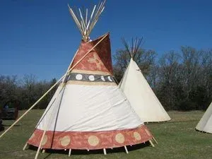 Two teepees on a grassy field, one red and white and one plain white, under a blue sky