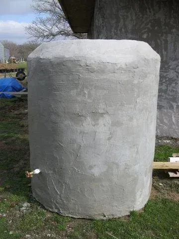 Large white cylindrical tank or container outdoors beside a building and grass
