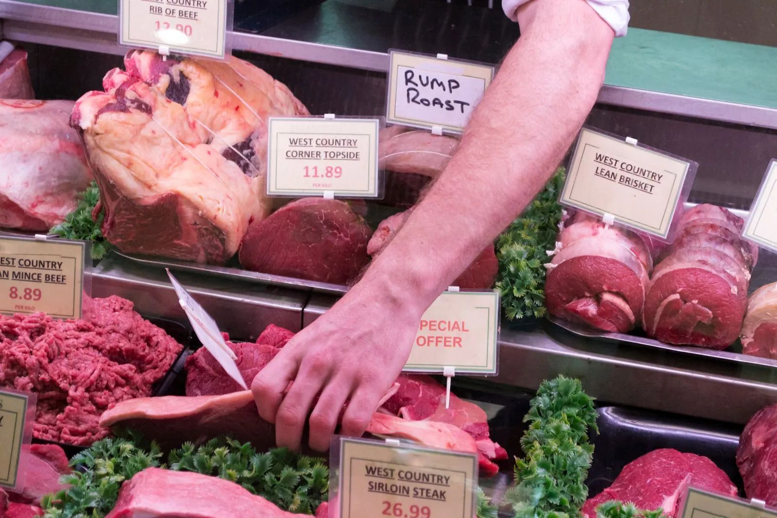 Butcher slicing meat at a deli counter with labeled cuts and displayed poultry and beef.