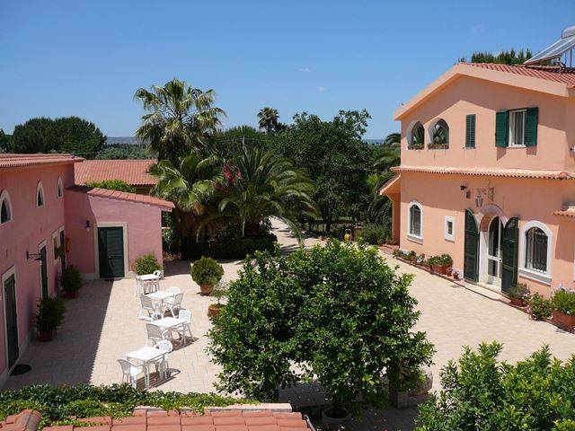 Edifici in stucco rosa con cortili, alberi e posti a sedere sotto un cielo azzurro e limpido.