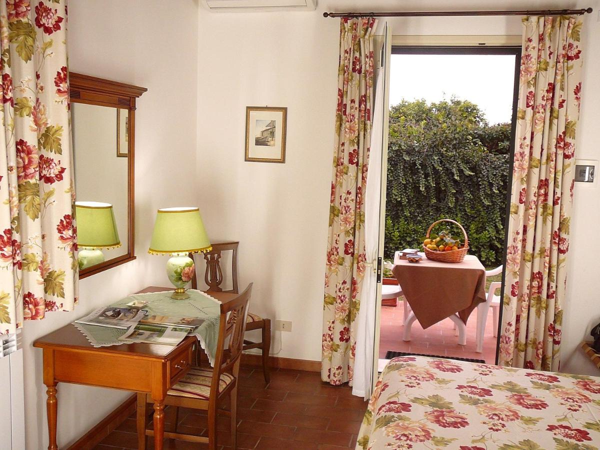 Una stanza con una porta aperta sul patio. Scrivania con specchio, tende floreali e biancheria da letto.
