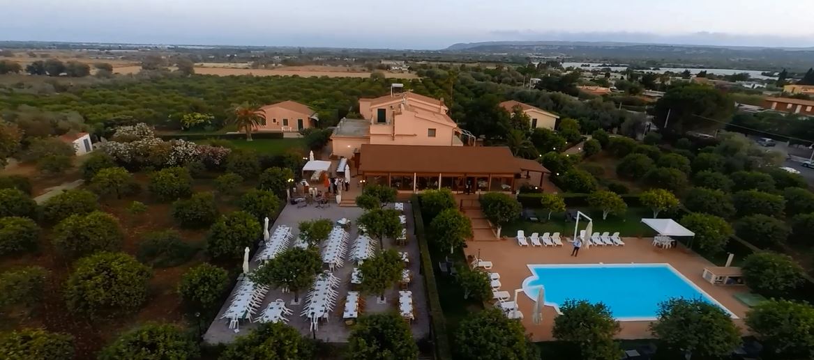 Vista aerea di un resort con piscina, tavoli da pranzo e paesaggio circostante.