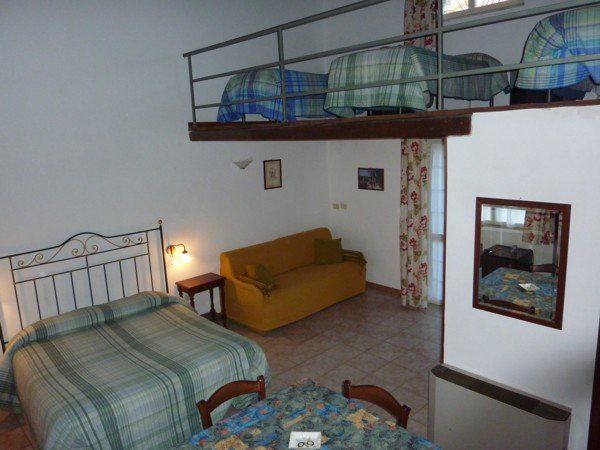Monolocale con soppalco, letto, divano, tavolo e letti nel soppalco con biancheria da letto a quadri verdi e blu.