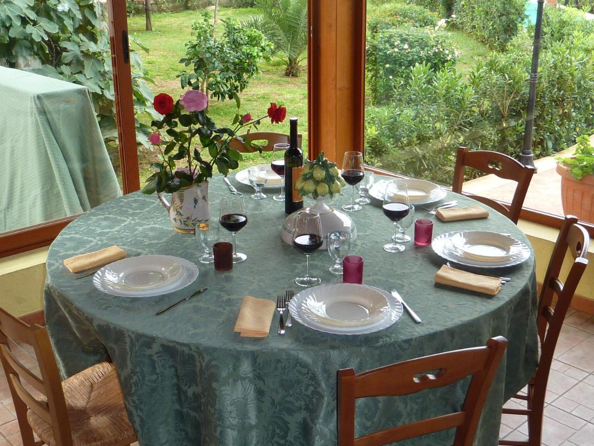 Un tavolo apparecchiato per sei persone con bicchieri da vino, piatti e vista su un rigoglioso giardino verde.