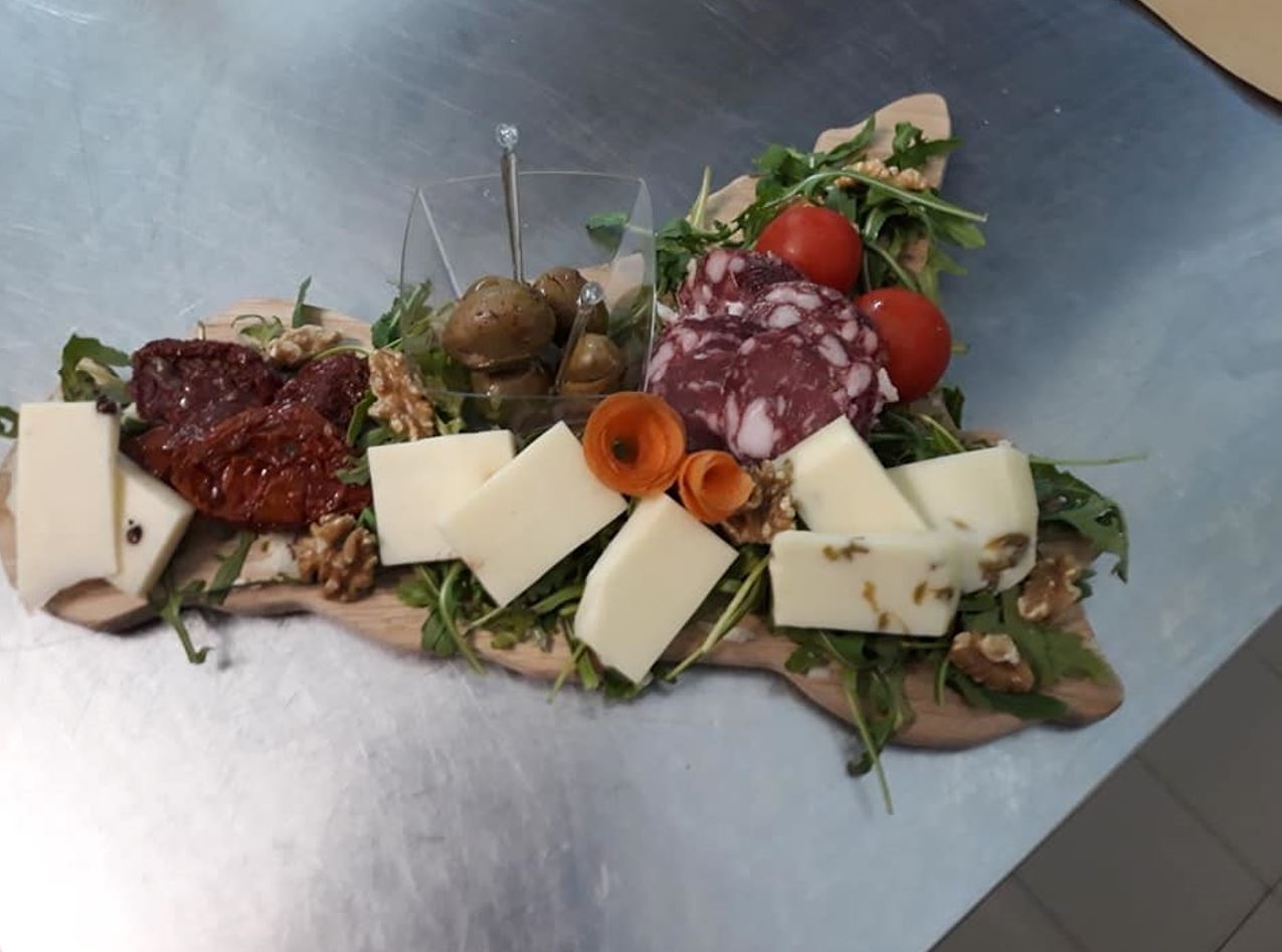 Tagliere di legno con formaggio, salame, pomodori, olive, noci e rucola.