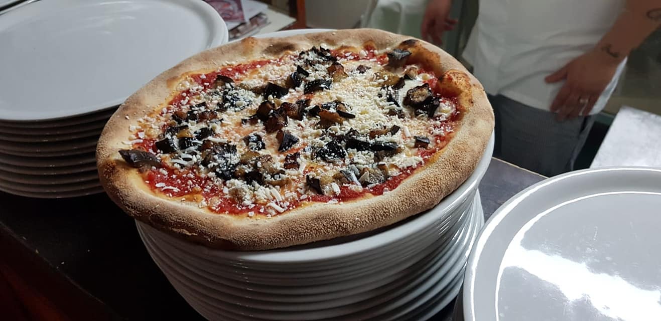 Pizza con funghi e formaggio su una pila di piatti bianchi.