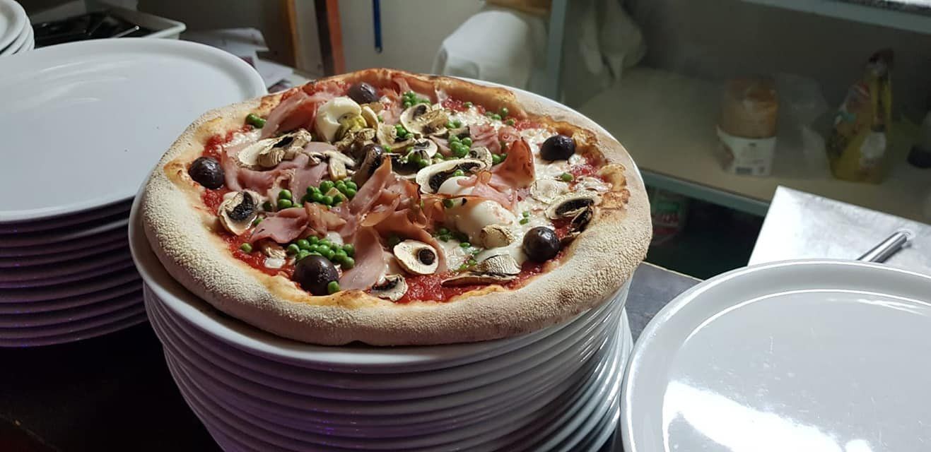 Pizza su una pila di piatti condita con olive, funghi e piselli, servita in un ristorante.