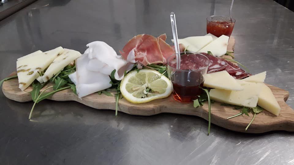 Tagliere di salumi con formaggi, carni, limone e gelatina servito su un vassoio di legno.