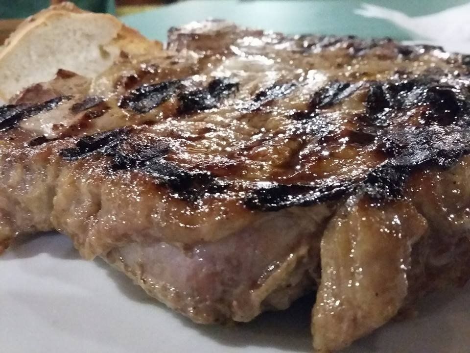 Bistecca alla griglia con i segni della griglia, servita su un piatto bianco accanto a una fetta di pane.