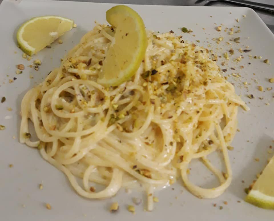 Spaghetti con salsa cremosa, guarniti con pistacchi e fette di limone su un piatto bianco.