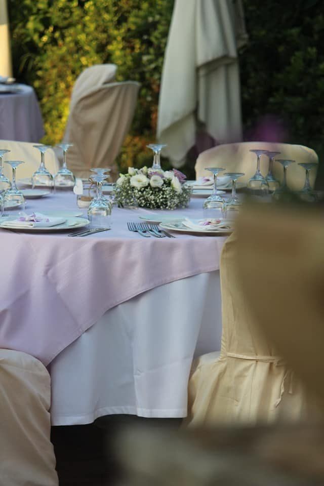 Tavolo da matrimonio all'aperto apparecchiato con piatti, bicchieri e centrotavola floreale. Tovaglie rosa chiaro e bianche.