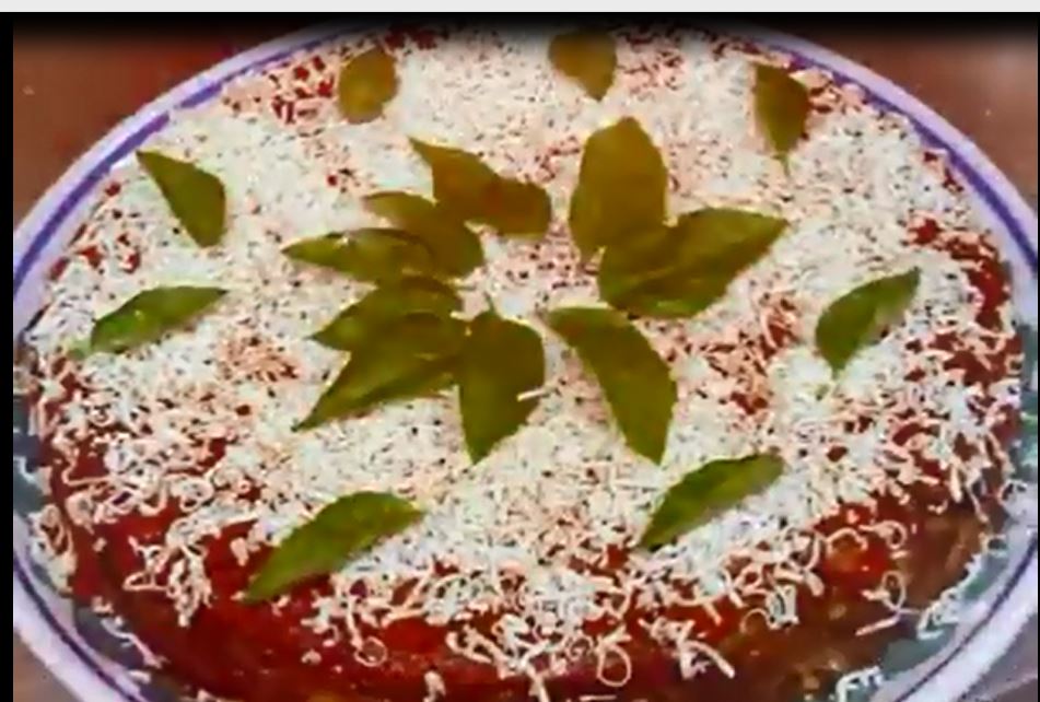 Torta rotonda ricoperta di formaggio grattugiato, salsa rossa e foglie verdi.