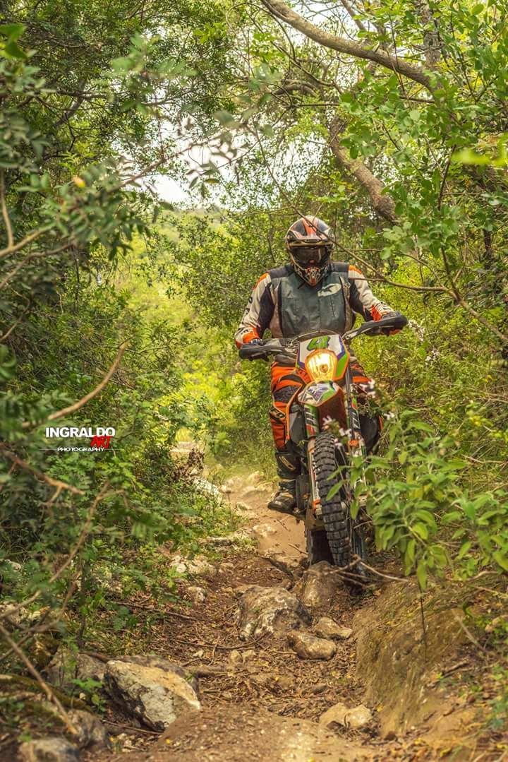 Uomo su una moto da cross arancione che percorre un sentiero roccioso attraverso una lussureggiante foresta verde.