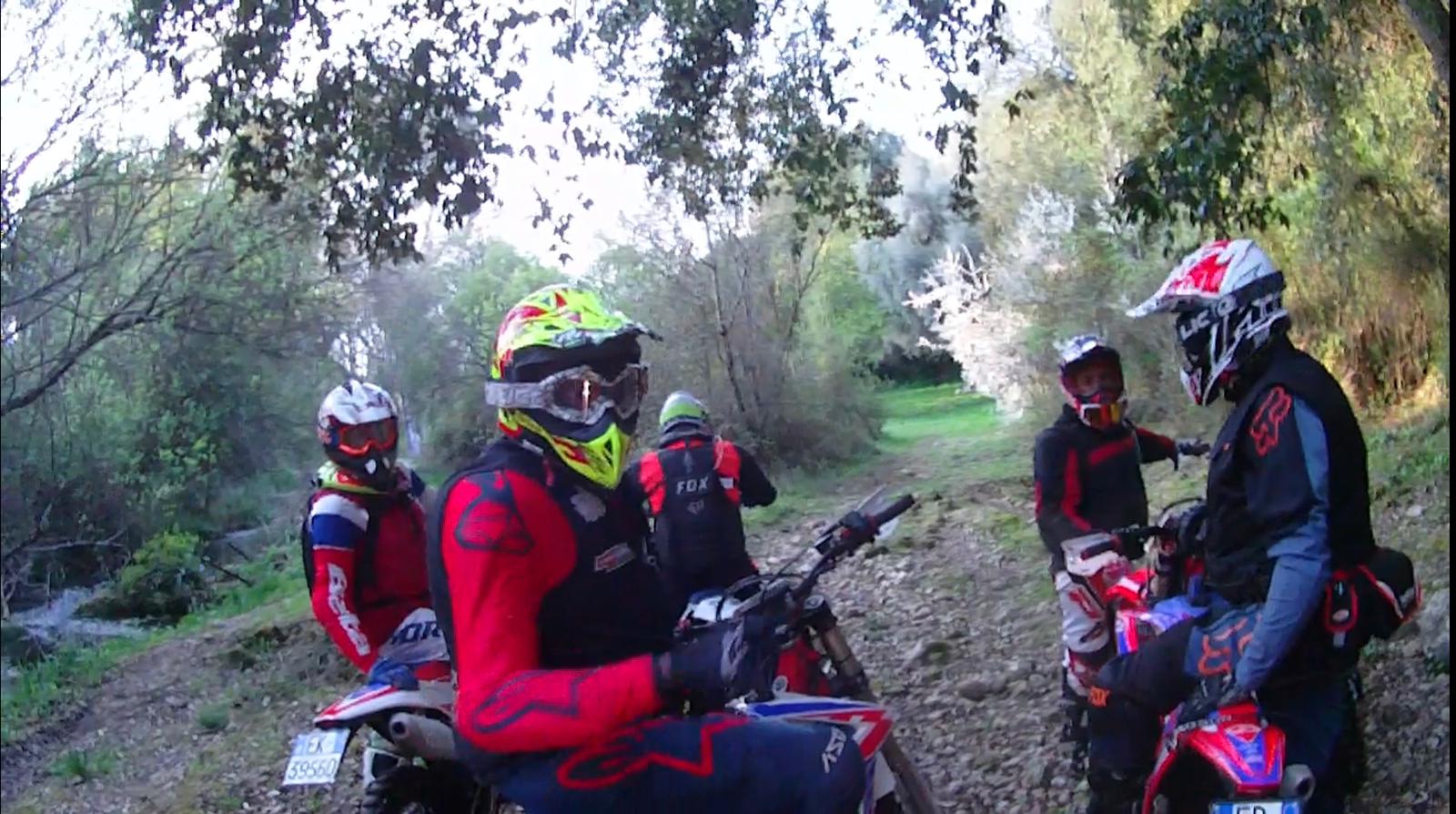 Motociclisti in tenuta da cross su un sentiero sterrato, in una zona boscosa, durante una pausa.