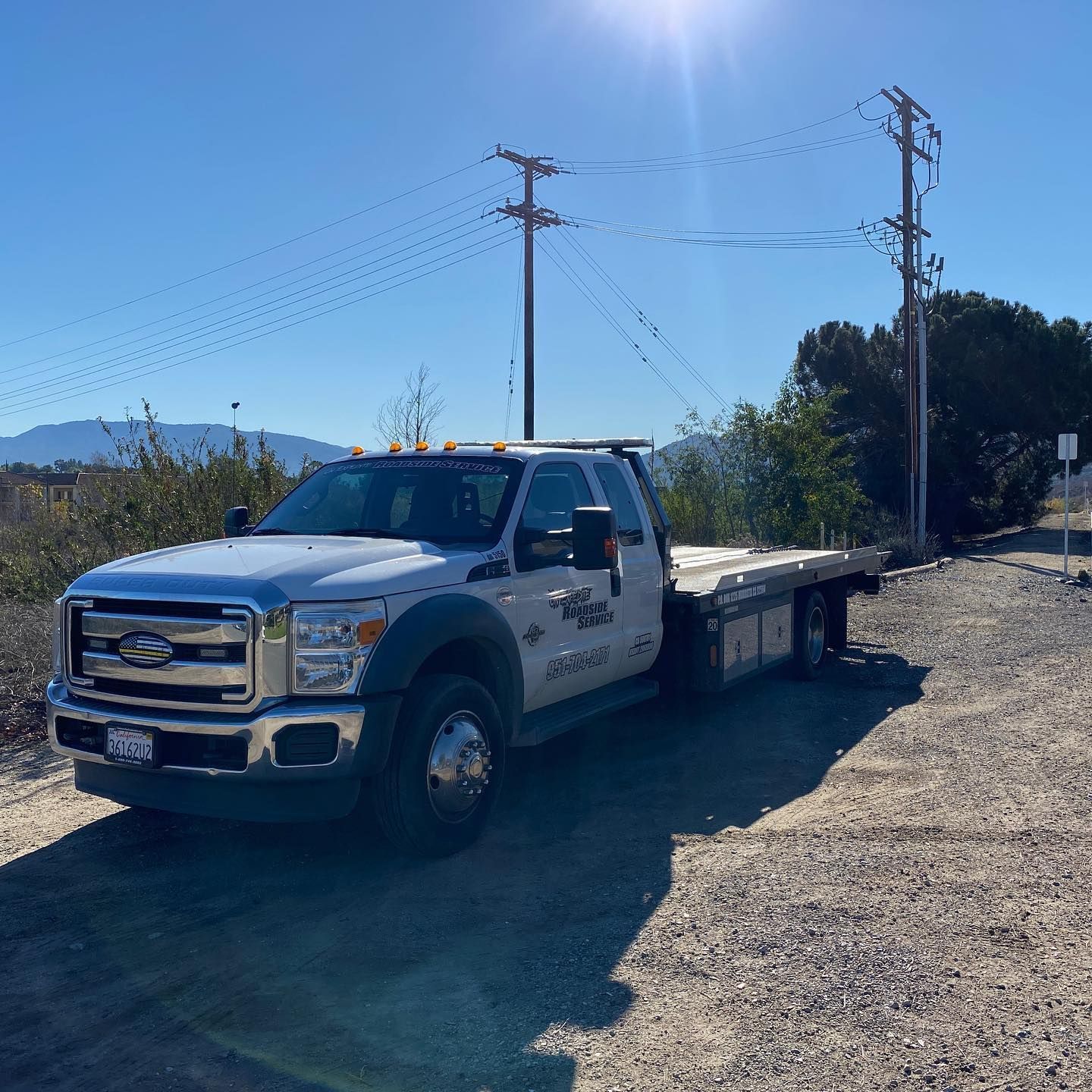 White tow truck parked on gravel road under a clear, sunny sky.