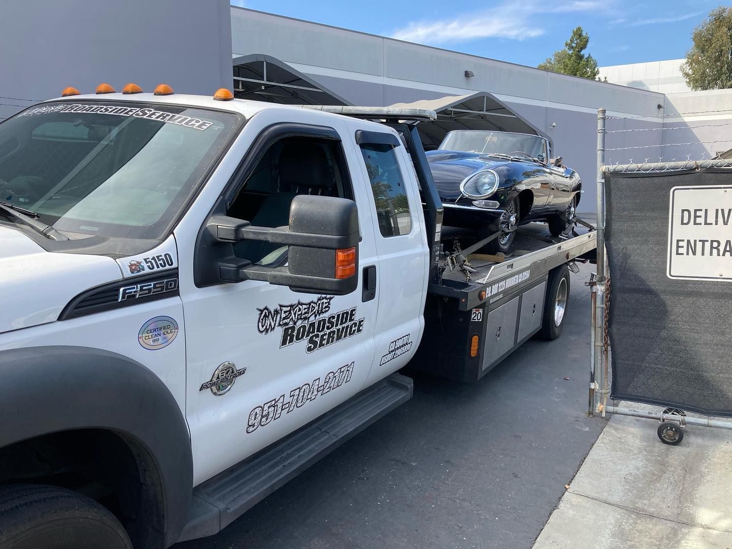 White tow truck transporting a black vintage car near a delivery entrance.