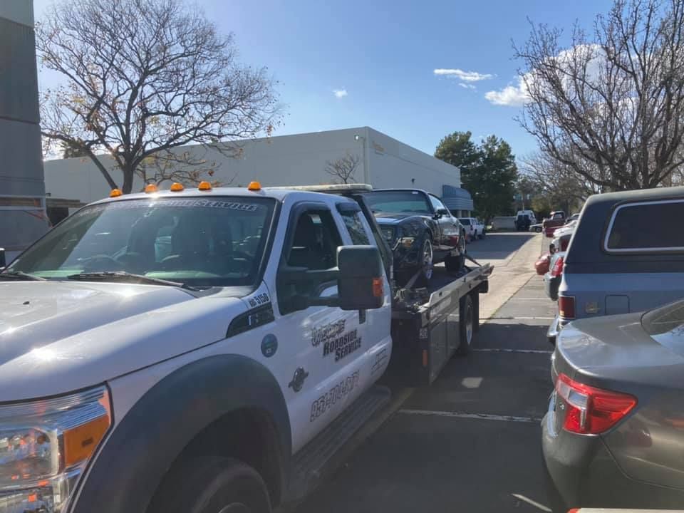 A tow truck with a car on its bed, parked in a lot on a sunny day.