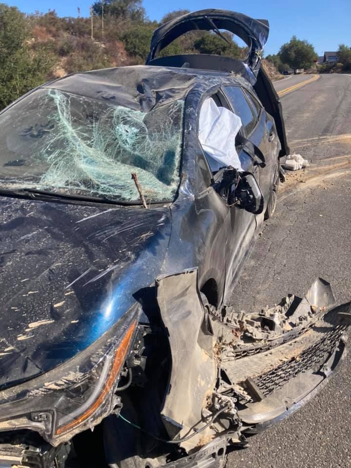 Damaged blue car on a road after an accident; broken windshield, crushed front.
