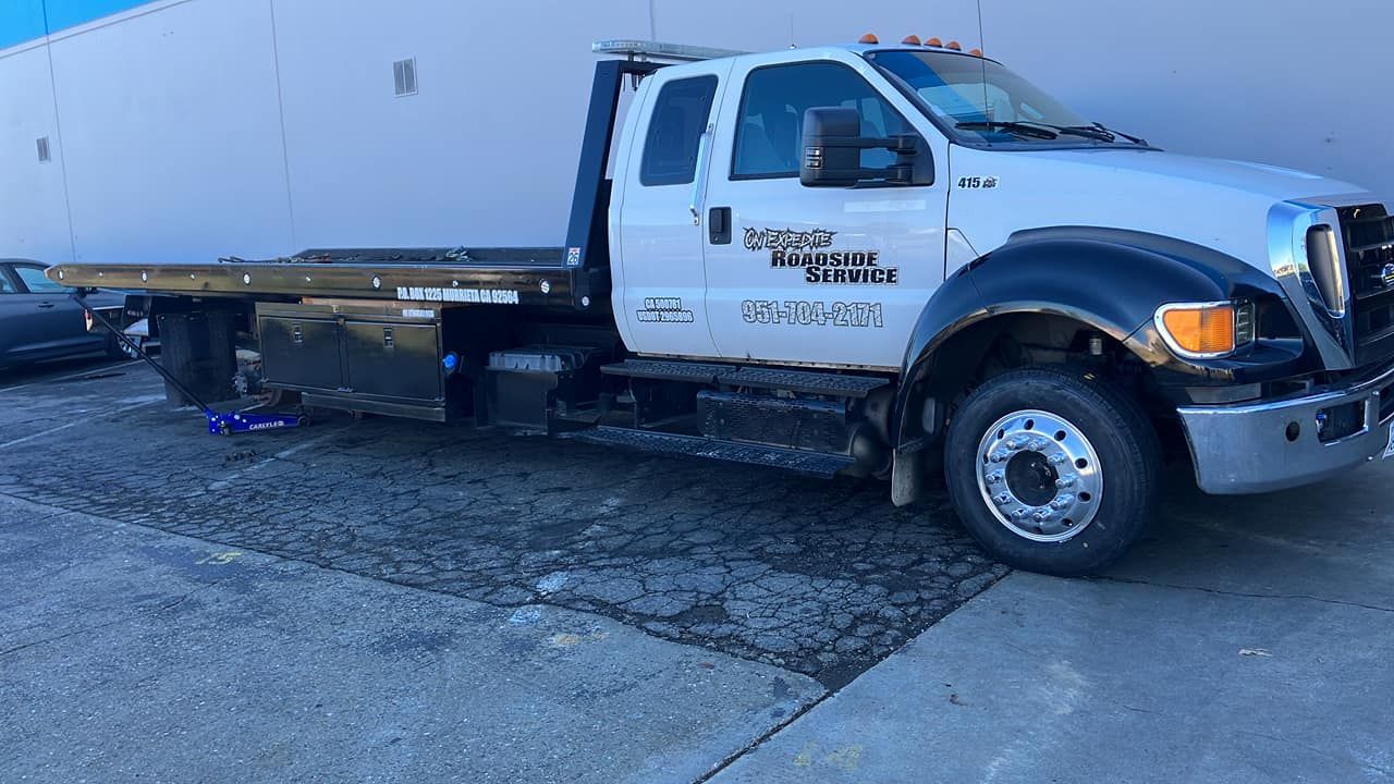 White tow truck parked on pavement with a blue jack near the tires, outdoors.