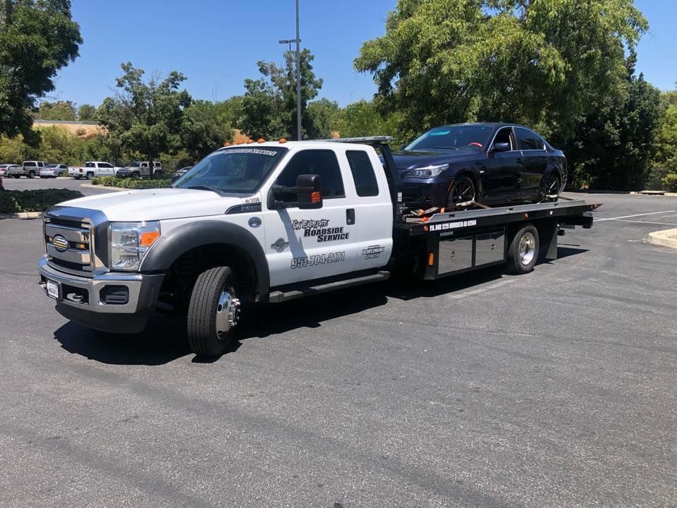 Tow truck with a black car on its flatbed, parked in a parking lot on a sunny day.