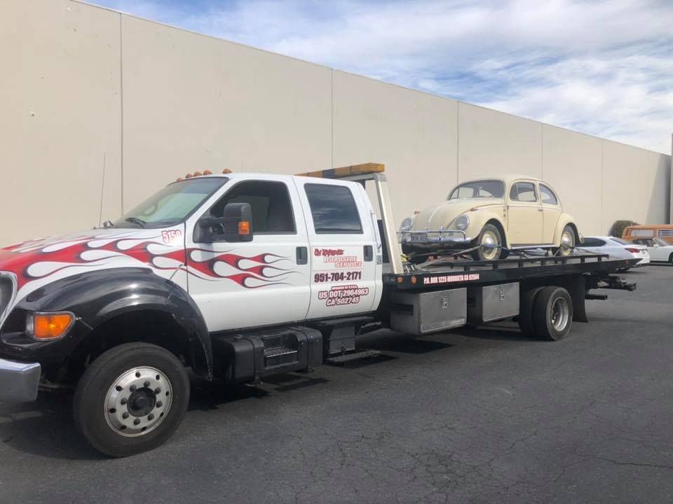 A tow truck with a vintage beige Volkswagen Beetle on its flatbed.
