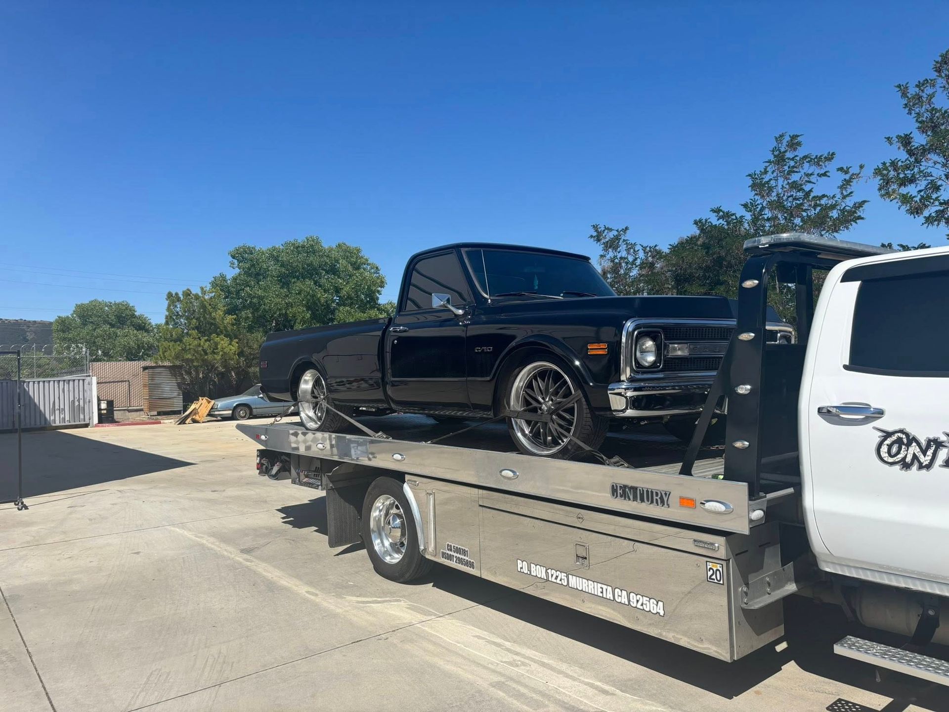 Black classic pickup truck on a tow truck in a sunny outdoor setting.