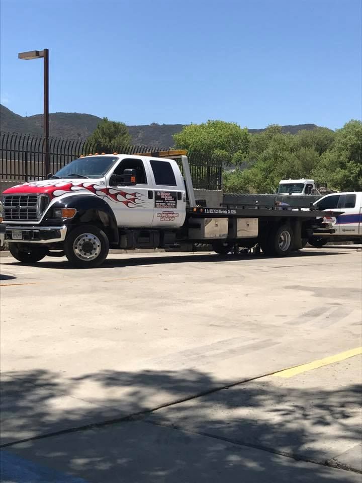 White tow truck with red accents, parked on asphalt on a sunny day.