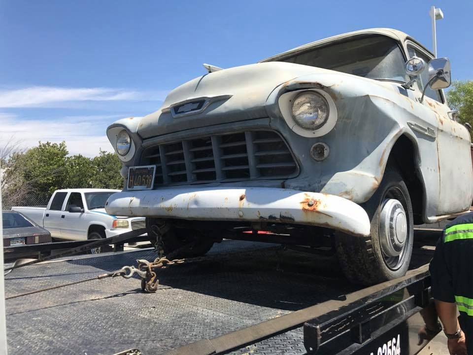 Old, rusty Chevy truck on a tow truck, outdoors on a sunny day.