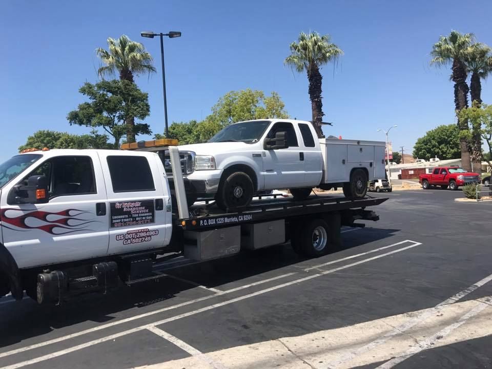 White tow truck carrying a white pickup truck on a sunny day in a parking lot.