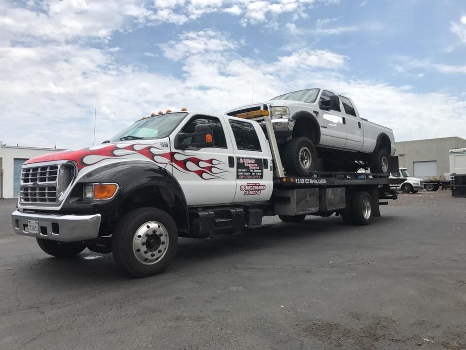 Tow truck with a white truck on its flatbed, outdoors, under a cloudy sky.
