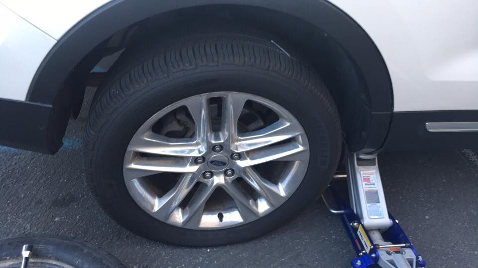 White car tire being lifted with a jack on an asphalt surface.
