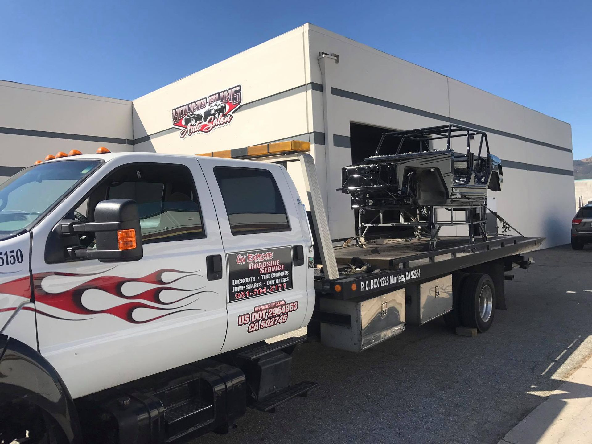 Tow truck with a black vehicle frame on the flatbed in front of a white building.