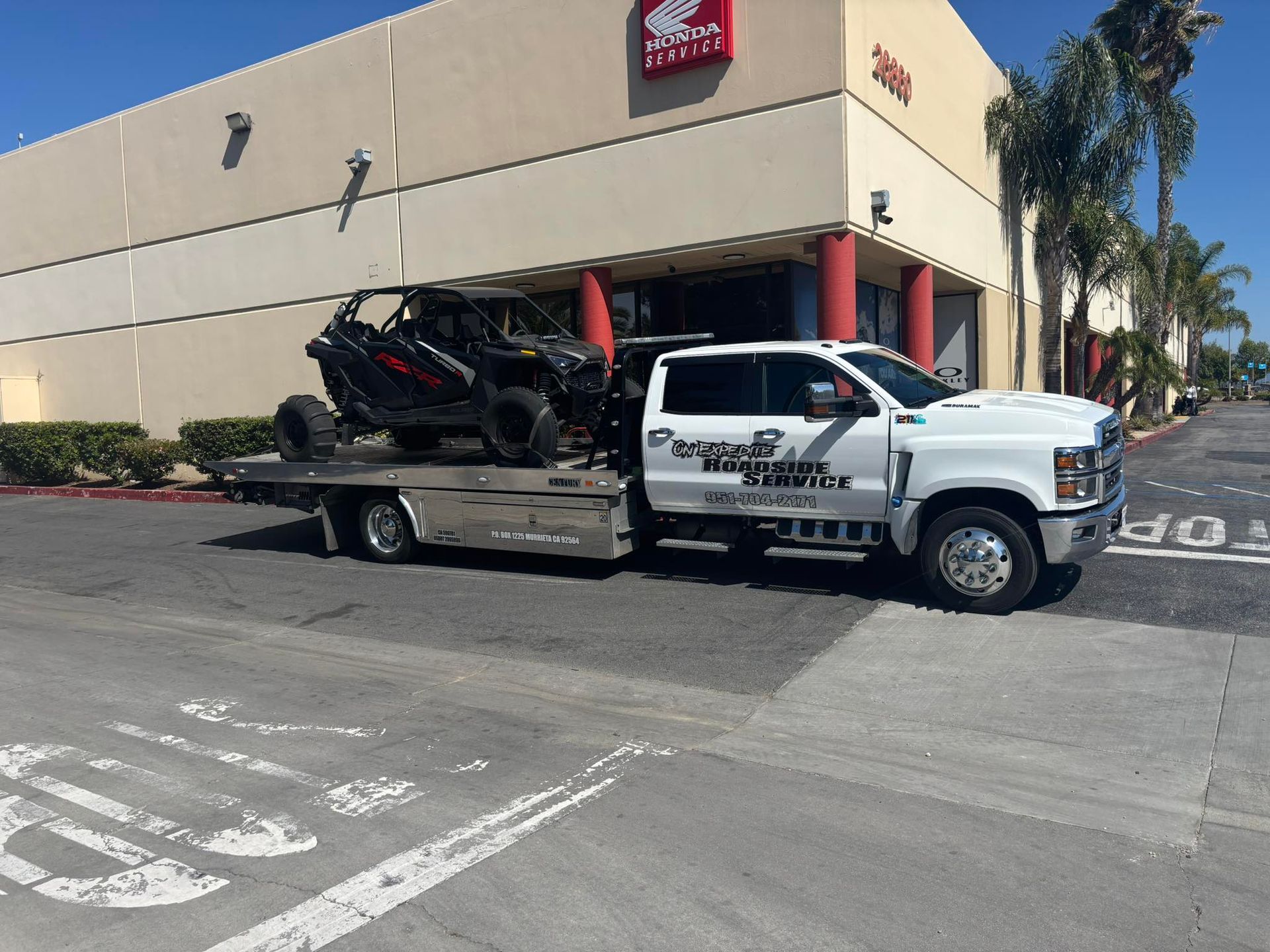 White tow truck with a black off-road vehicle, parked in front of a Honda dealership.
