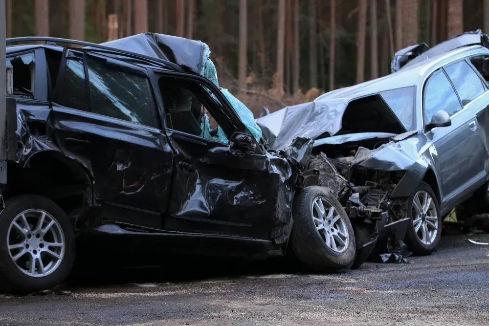 Two crushed cars after a head-on collision, front ends smashed on a road.