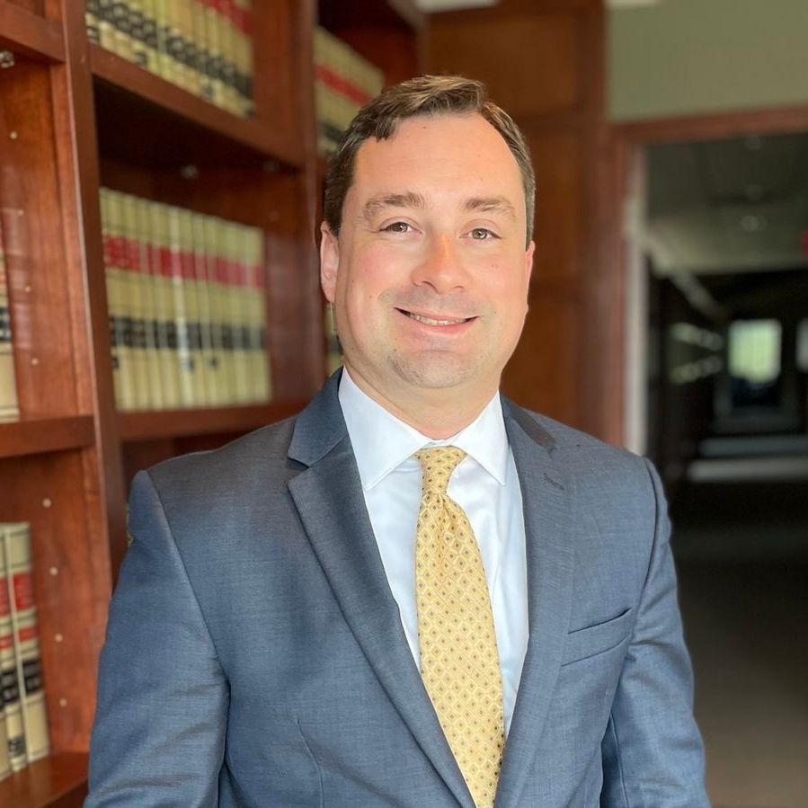 Man in a blue suit and yellow tie standing in a wood-paneled library hallway.