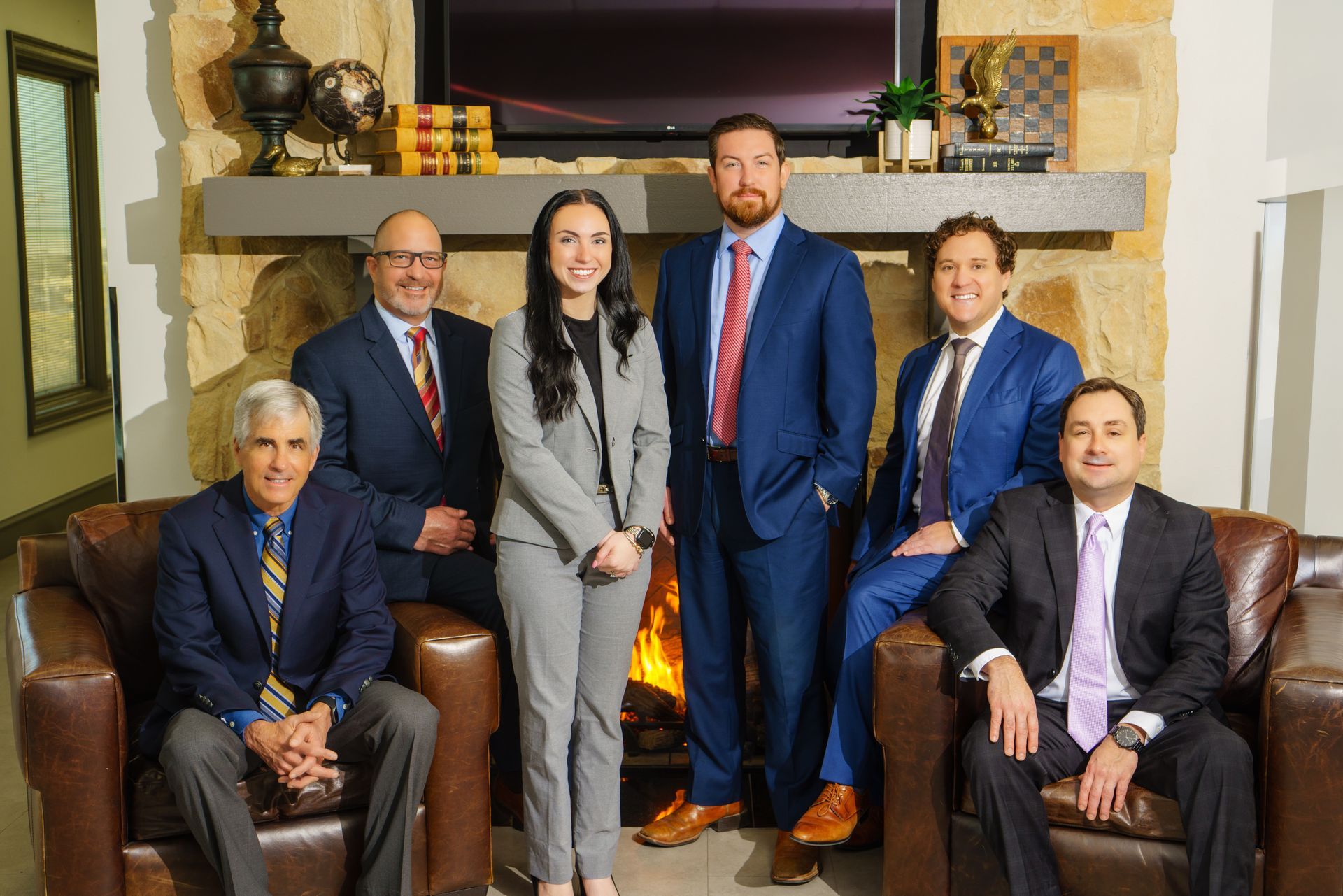 Six people posed in a living room with a fireplace and TV, dressed in business attire.