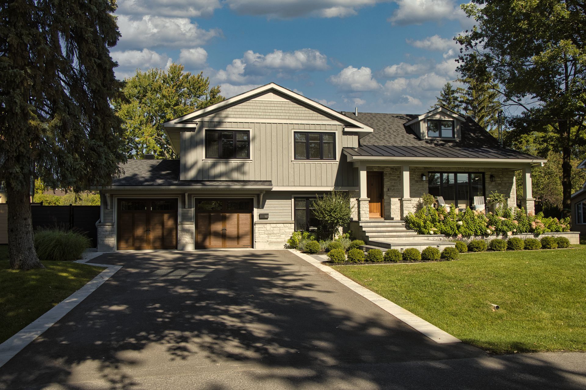 Modern gray house with dark trim, driveway, and landscaping on a sunny day.