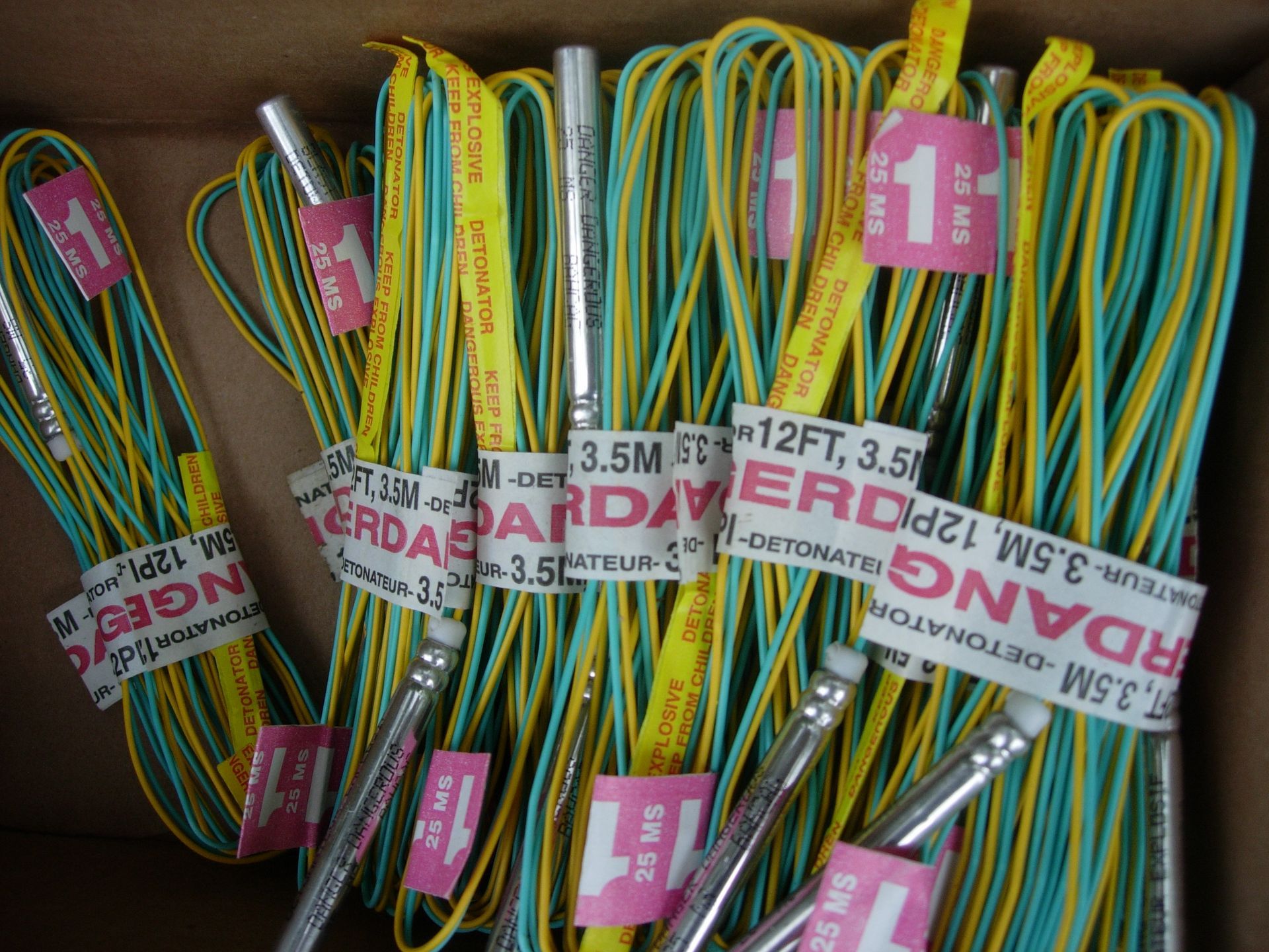 Bundles of wires with labels and metal tubes inside a cardboard box. Yellow, blue, and white wires.