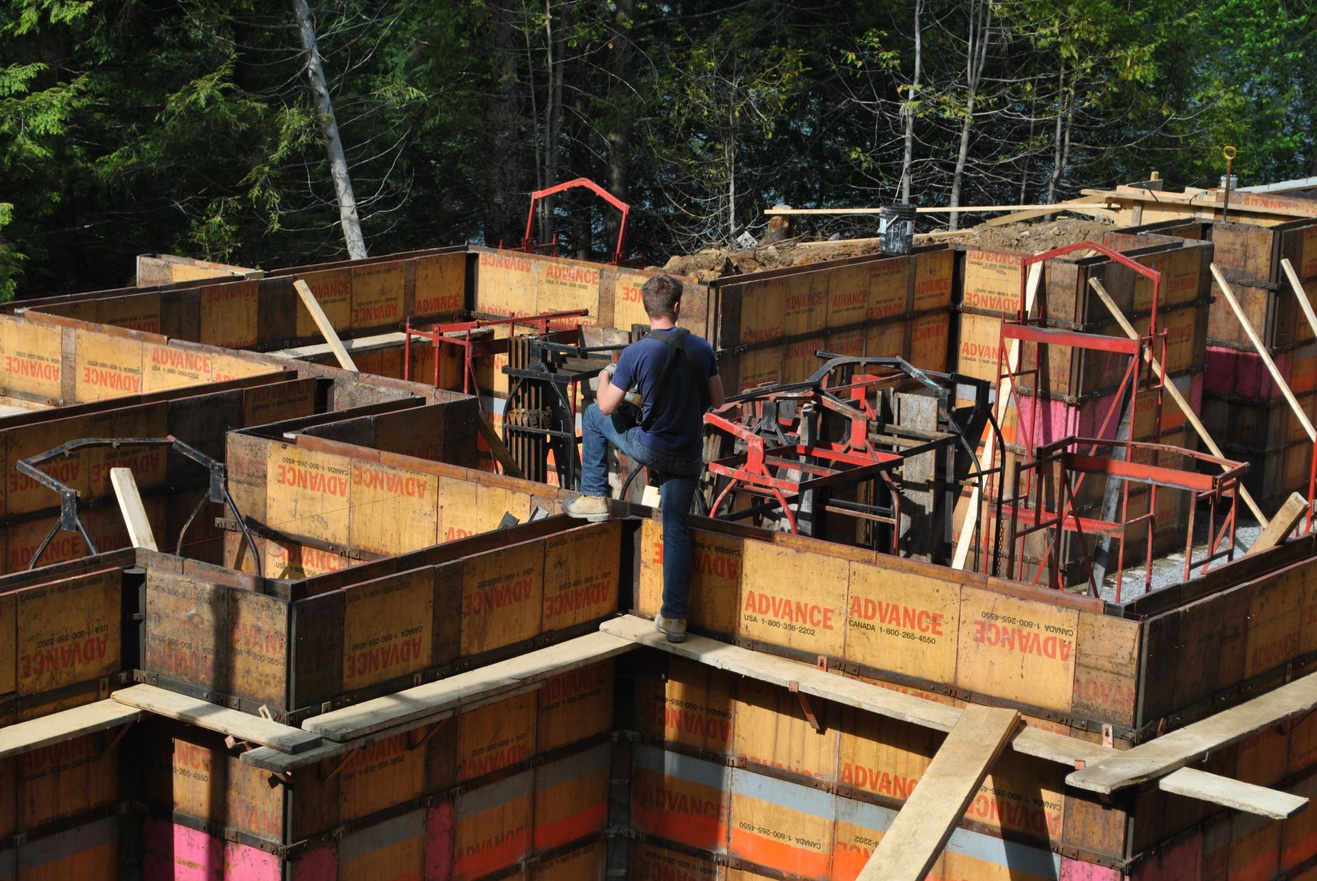 Construction site with wooden forms for concrete walls; person standing atop forms.